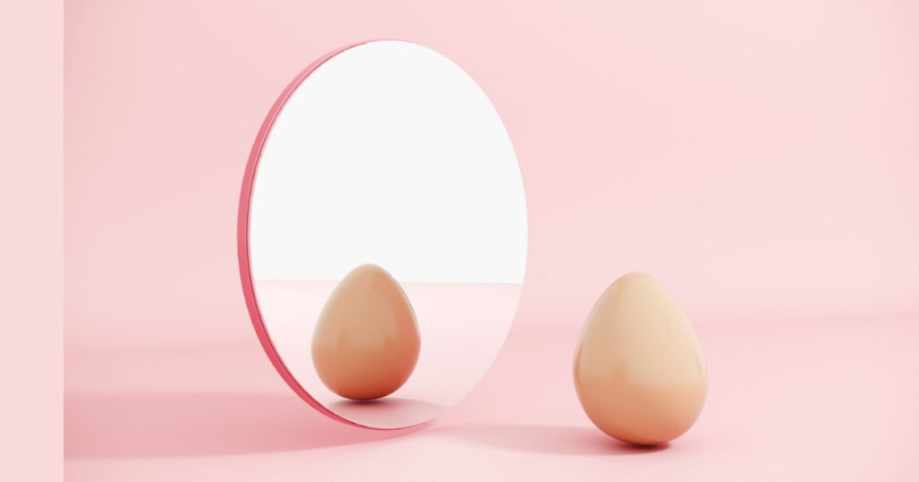 Egg reflecting in round mirror on pink background.