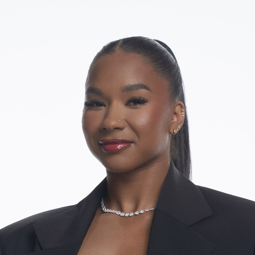 Woman in suit with necklace, hair tied back.