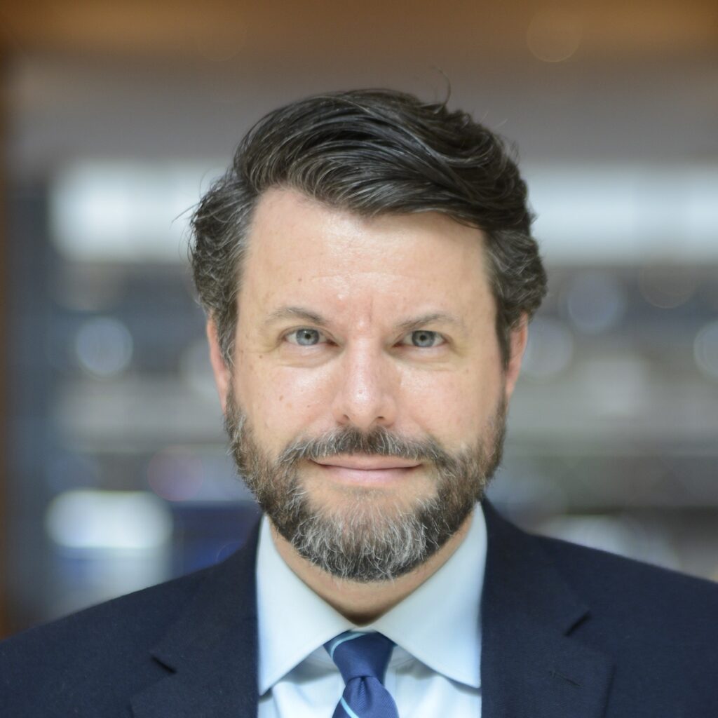 Man in suit with beard smiling indoors.