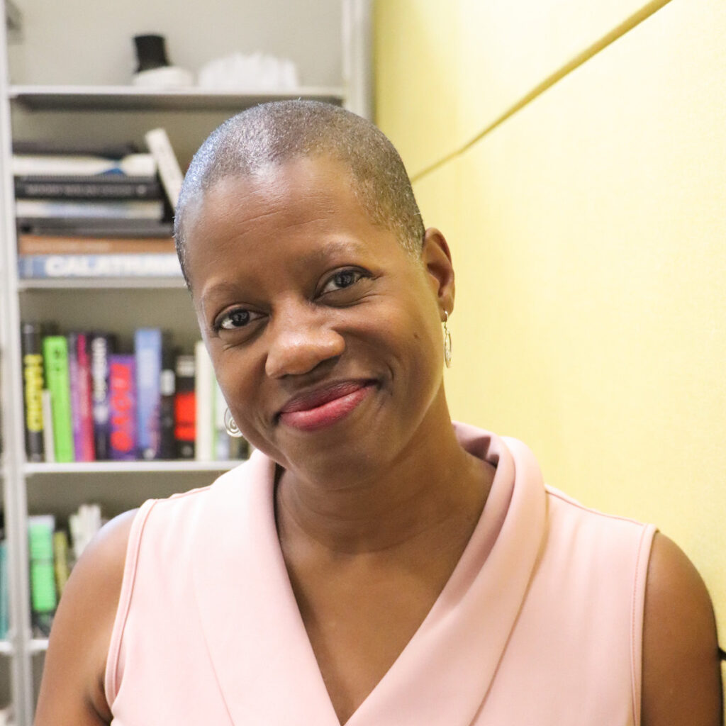 Smiling person in a pink top near bookshelves.