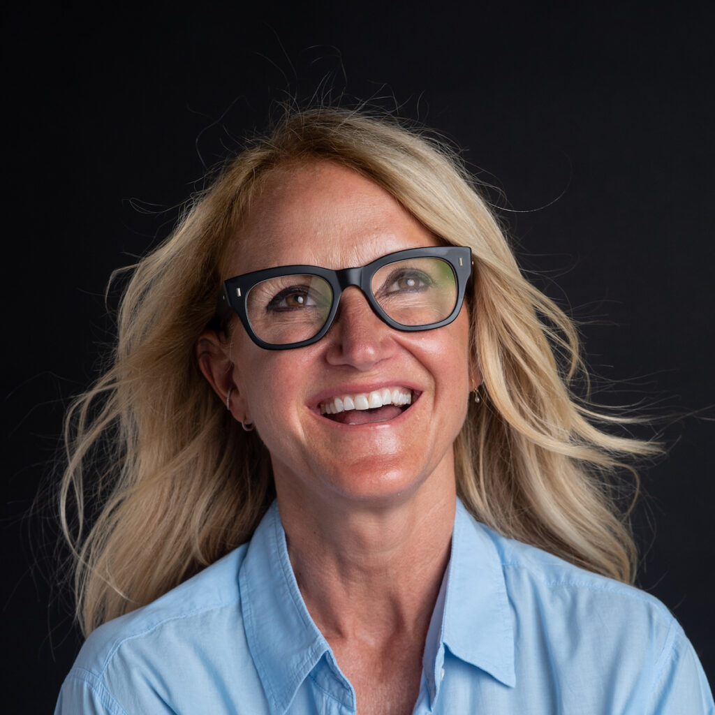 Smiling woman with glasses on black background.