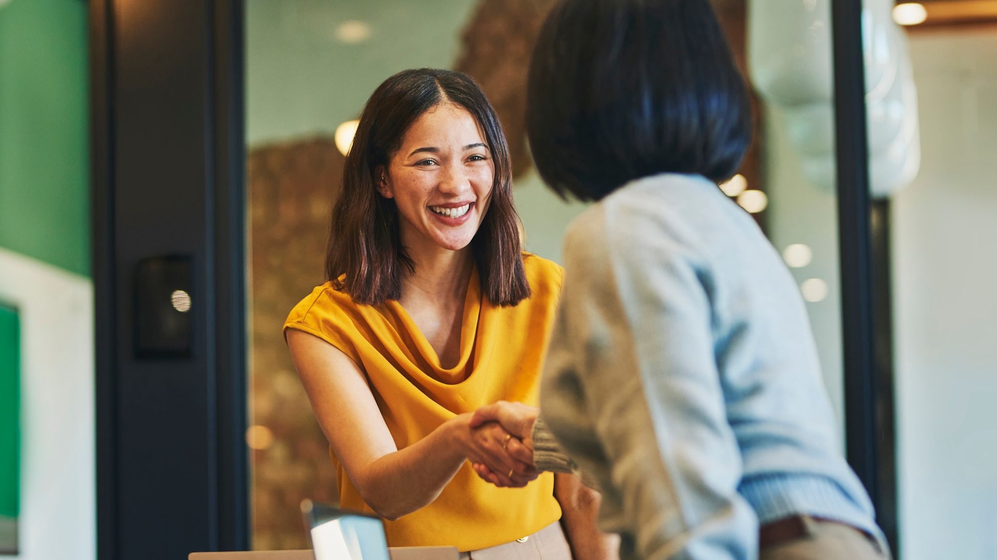 Two people shaking hands in office setting.
